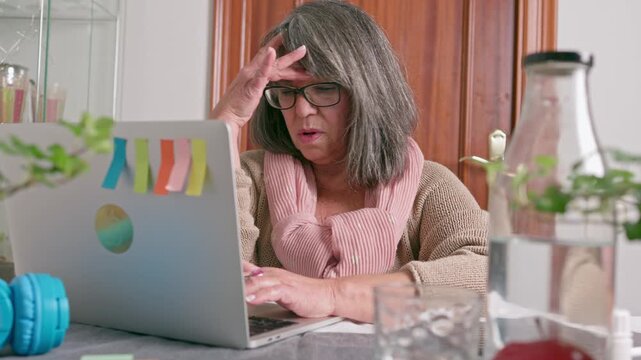 Overwhelmed senior woman working from home experiencing a severe headache, taking off her glasses and rubbing her forehead while feeling tired, stressed and suffering  eye strain.burnout and overwork.