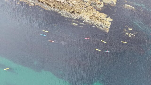 Top down aerial drone view of colourful kayaks paddling in clear ocean waters near rocky coastline in Mullaghmore, County Sligo, Ireland.