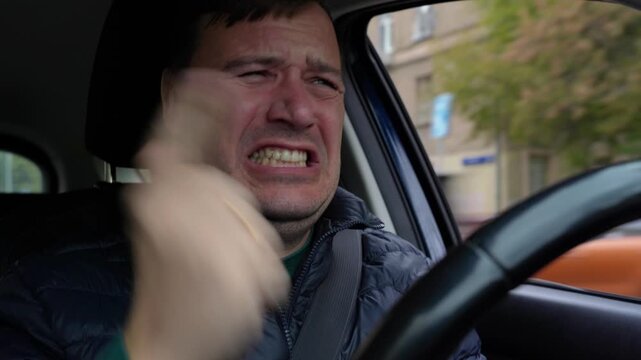 Man driving car experiences moment of extreme disgust or distress while on road, grimacing intensely before regaining composure.