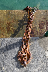 Heavy rusty iron mooring chain anchored to a stone dock in the turquoise harbor water of Portofino, Liguria, Italy © Simona Sirio
