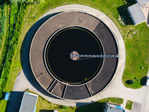 Aerial view of the circular sedimentation tank at the Sloka wastewater treatment plant, featuring floating solar panels, surrounded by green grass and buildings in Jurmala, Latvia.