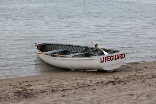 Lifeguard rowboat resting on the shore of a sandy beach beside calm lake water, ready for emergency rescue operations.