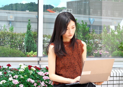 屋外テラスのベンチでノートパソコンを開き仕事をする若い女性