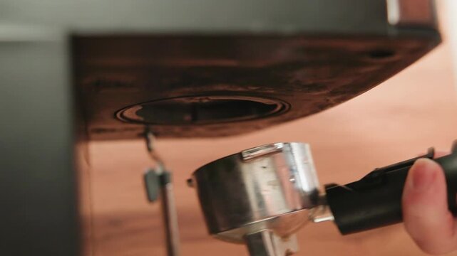 Close-up low-angle view shows hand gripping black handle to tighten cylindrical chrome fastener beneath black table edge, with clear adjustment motion, hardware detail, and indoor workshop setting