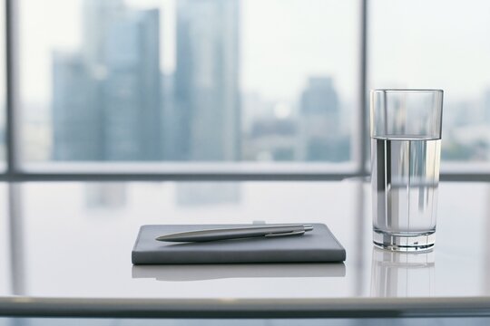 Minimalist Office Workspace with Gray Notebook, Metallic Pen and Glass of Water