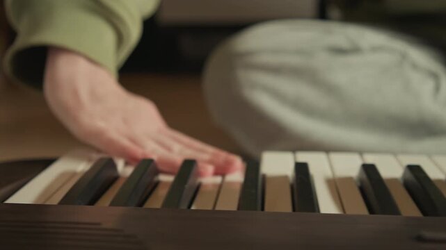Low angle view of hands actively playing electronic keyboard, fingers pressing black and white keys in warm indoor light, showing rhythmic movement, focused touch, and subtle motion blur