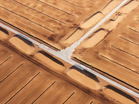Aerial view of an industrial peat extraction site featuring parallel drainage ditches and a central access road across the harvested peatland, Latvia.