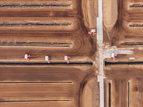 Aerial view of industrial peat extraction machinery operating on large brown fields with parallel rows for horticultural production in Latvia.
