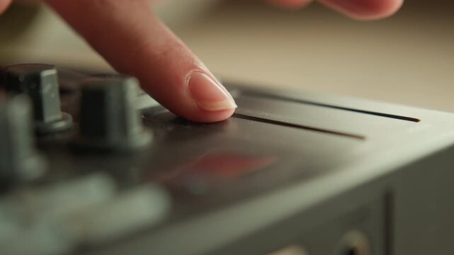 Low-angle view of index fingertip moving across touch strip on dark control console, creating slight blur while adjacent knobs and buttons suggest hands-on audio or device operation
