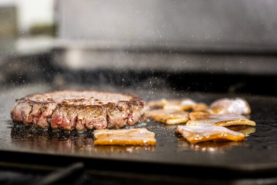 Beef patty and bacon cooking on hot griddle