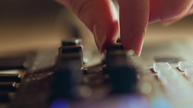 Close view of fingers moving channel fader on audio mixing console, with warm studio light, matte controls, textured metal surface, and precise tactile sound adjustment in professional workspace