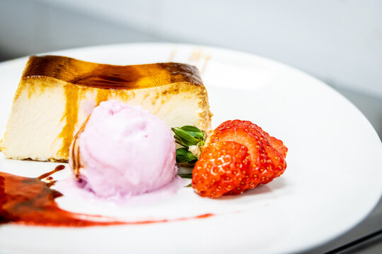 Dessert plating a slice of cheesecake with red fruit, raspberry ice cream, and jam