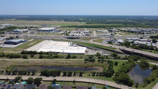 Elongated drainage ponds buffer single family backyards near Interstate 35W across DFW suburbs. Highway overpasses, distribution warehouses border residential blocks, Burleson, Texas