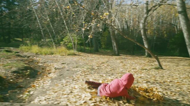 Boy falling backward into a pile of golden autumn leaves and laughing