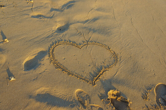 A heart drawn in the warm sand at sunrise, capturing a moment of love by the seaside.