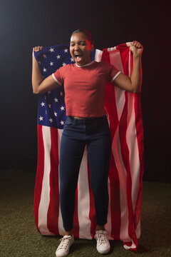 African American woman standing on studio turf holding US flag wearing red ringer tee and sneakers