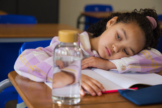 African American schoolgirl in plaid jacket resting on desk in class with water bottle, copy space
