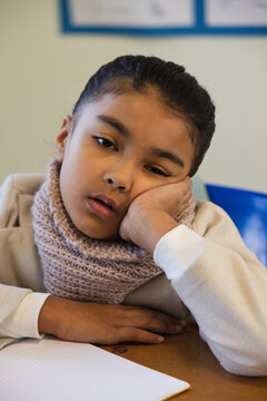 African American child sitting and resting on hand at desk in classroom with scarf and notebook