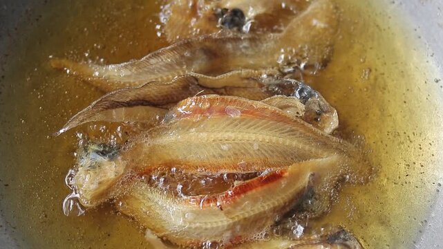 Fried dried sole fish in boiling oil on wok. 