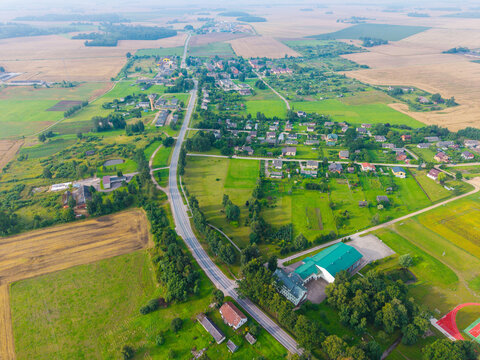 Aerial view of the rural village of Jaunberze featuring green fields, a winding road, and scattered houses in Jaunberze, Dobele Municipality, Latvia.