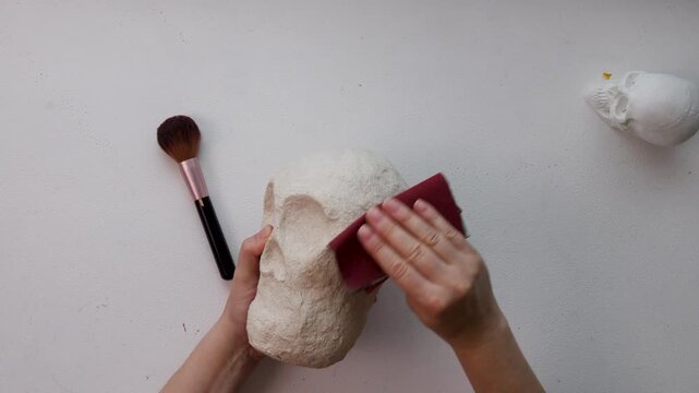 Smoothing a handmade papier-m&acirc;ch&eacute; calavera skull in a DIY home workshop setup