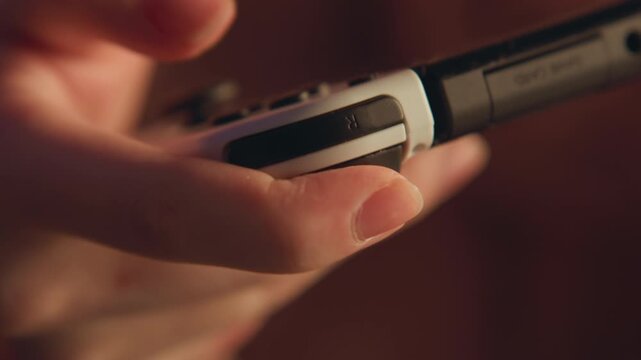 Index finger pressing elongated black control strip on compact handheld device, fingertip contact and slight motion blur showing deliberate input while thumb stabilizes grip in warm low-key light
