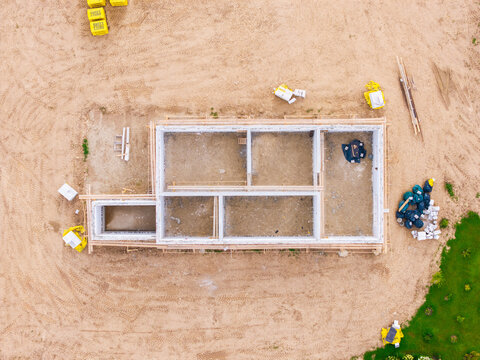 Aerial view of a building foundation under construction with concrete walls and scattered construction materials on a dirt site in Jaunberze, Dobele Municipality, Latvia.
