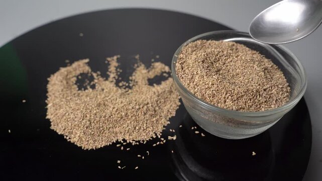 Close-up View of Carom Seeds (Trachyspermum ammi) Being Poured from a Spoon onto a Black Surface
