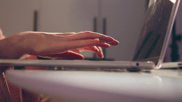 Low-angle tight crop showing hands and wrists typing on laptop placed on light desk, fingers extended and blurred between keystrokes to convey continuous rapid motion and focused work