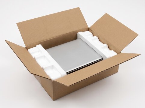 Open cardboard box with modern silver laptop computer safely packed inside white styrofoam protective foam inserts on clean white background