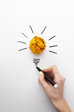 human hand drawing a light bulb on paper. flat lay abstract composition with innovation elements. Human finger touches a bright yellow crumpled paper ball shaped like a light bulb drawn on a textured.