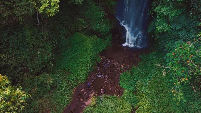 Aerial drone view of Coban Kaca waterfall flowing through dense tropical forest in Malang, East Java, Indonesia. The narrow waterfall cascades between lush green trees, creating a peaceful and seclude