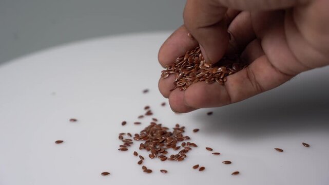 Close Up Hand Sprinkle Flaxseed on White Surface for Healthy Lifestyle and Cooking