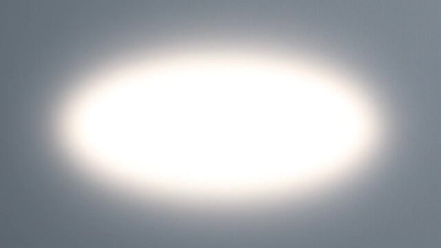 Bright white oval light glow centered on a soft grey gradient background for minimalist design and digital presentation