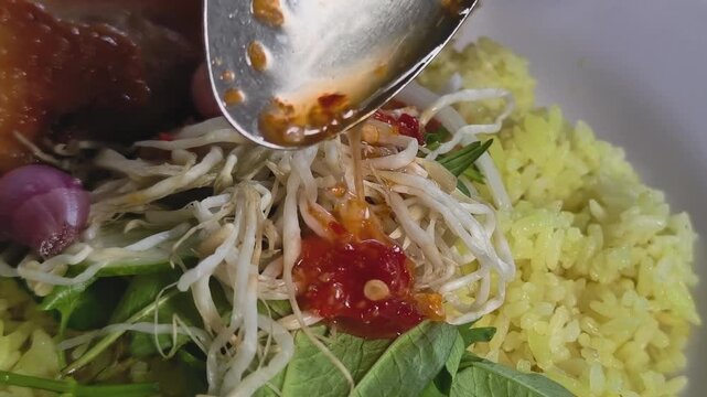 Macro close-up shot of pouring chili dipping sauce over Vietnamese Phu Yen chicken rice with turmeric rice and pickled shallots