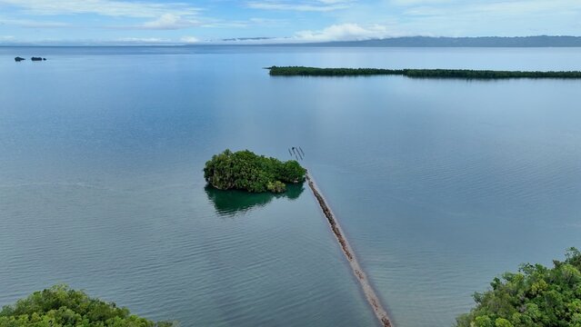 Aerial view of Los Haitises Trail featuring a small lush island surrounded by calm turquoise waters and a narrow stone path extending into the sea in Sanchez, Samana, Dominican Republic.