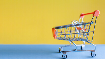 Miniature shopping cart positioned on a blue surface against a bright yellow background, suitable for retail and e-commerce imagery © Anat art