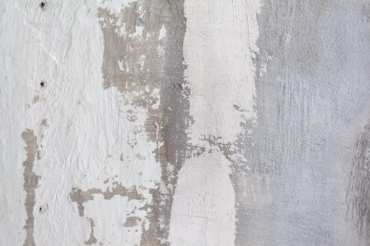 Textured wall features peeling paint in white and gray tones, exposing layers of plaster and concrete, creating a weathered appearance