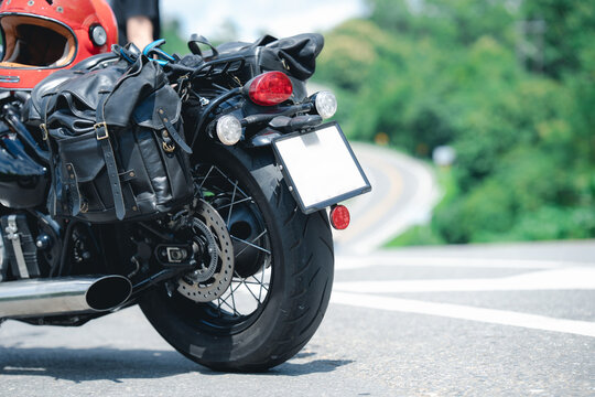 Motorcycle with leather saddlebag and red helmet rests on scenic road, evoking sense of adventure