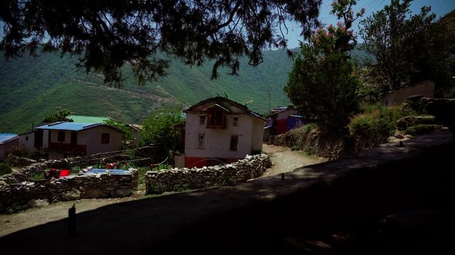 Traditional white and red mud brick house with wooden window and stone fence along dirt path in Nepali hill village
