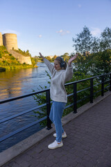 Fototapeta premium Woman with headphones dancing joyfully on riverside walkway by fortress