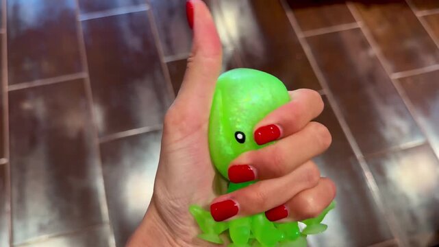Female hand squeezing a shiny green octopus squishy toy. Horizontal 4K close-up video showcasing tactile sensory play, stress relief, satisfying texture, relaxation and colorful fidget toy concept