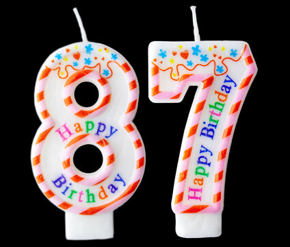 Number eighty seven shaped birthday candle with colorful sprinkles and Happy Birthday text isolated on a black background