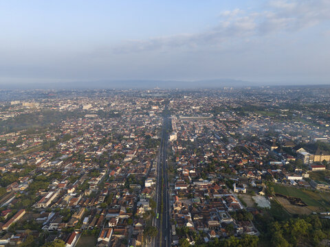 Aerial view of Yogyakarta City featuring dense urban residential rooftops and a central road stretching towards the horizon in Kecamatan Depok, Daerah Istimewa Yogya, Indonesia.