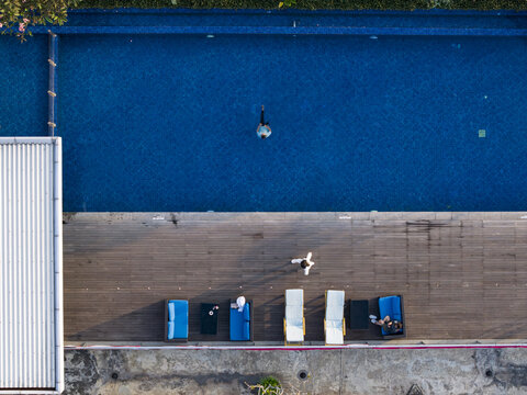 Aerial view of INNSiDE by Melia Yogyakarta featuring a blue swimming pool with a swimmer, a wooden deck with lounge chairs, and guests in Kecamatan Depok, Daerah Istimewa Yogya, Indonesia.