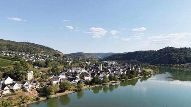 Aerial drone view of Bullay on the Moselle River in Rhineland-Palatinate, Germany, featuring the riverside village, church, river bend and surrounding forested hills in the scenic Moselle Valley.