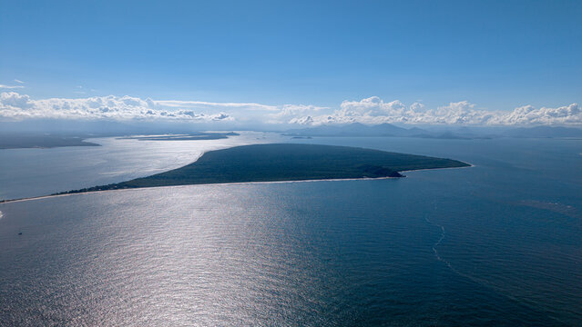 Aerial view of Ilha do Mel surrounded by the Atlantic Ocean under a clear blue sky with scattered clouds in Paranagua, State of Parana, Brazil.