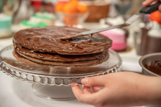 Homemade chocolate cake being covered with chocolate ganache on a glass cake stand during baking and dessert preparation.