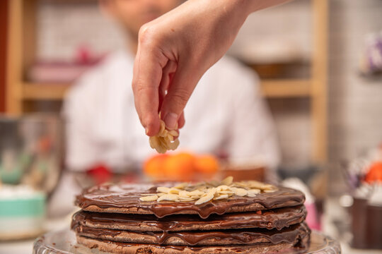 Hand decorating a homemade chocolate cake with sliced almonds and chocolate frosting during dessert preparation.