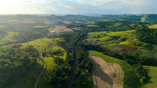 Aerial view of the BR-277 highway winding through lush green hills, agricultural fields, and patches of forest in the rural landscape of Laranjeiras do Sul, Parana, Brazil.